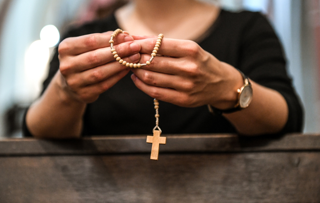 Hände einer knieenden Frau in einer Kirche halten einen Rosenkranz